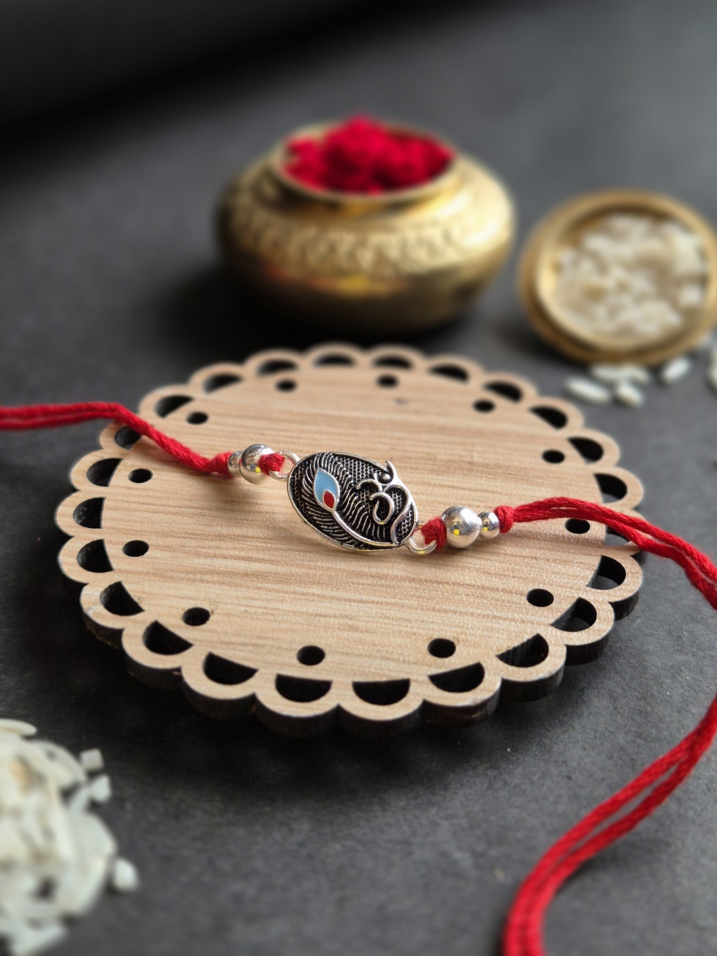 Divine Om Silver Rakhi featuring an intricate Om pendant on a wooden base, decorated with red threads and auspicious rice.