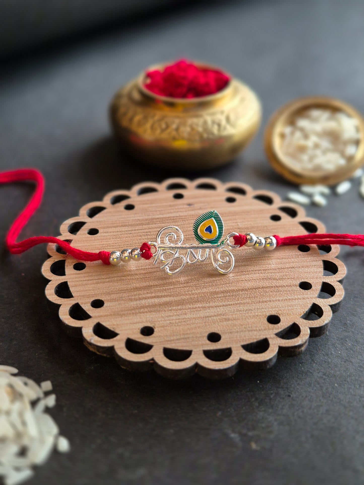 Krishna Sterling Silver Rakhi with peacock feather on decorative wooden surface for Raksha Bandhan celebration.