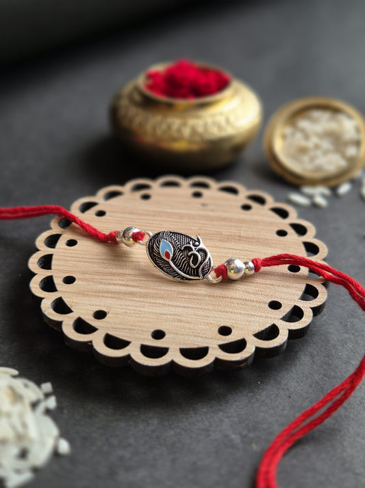 Divine Om Silver Rakhi featuring an intricate Om pendant on a wooden base, decorated with red threads and auspicious rice.