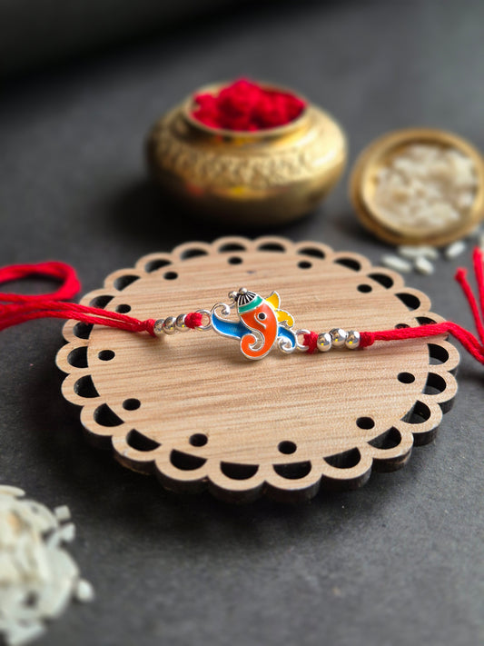 Vibrant Ganesha sterling silver rakhi on decorative wooden plate with traditional elements, symbolizing love and protection.