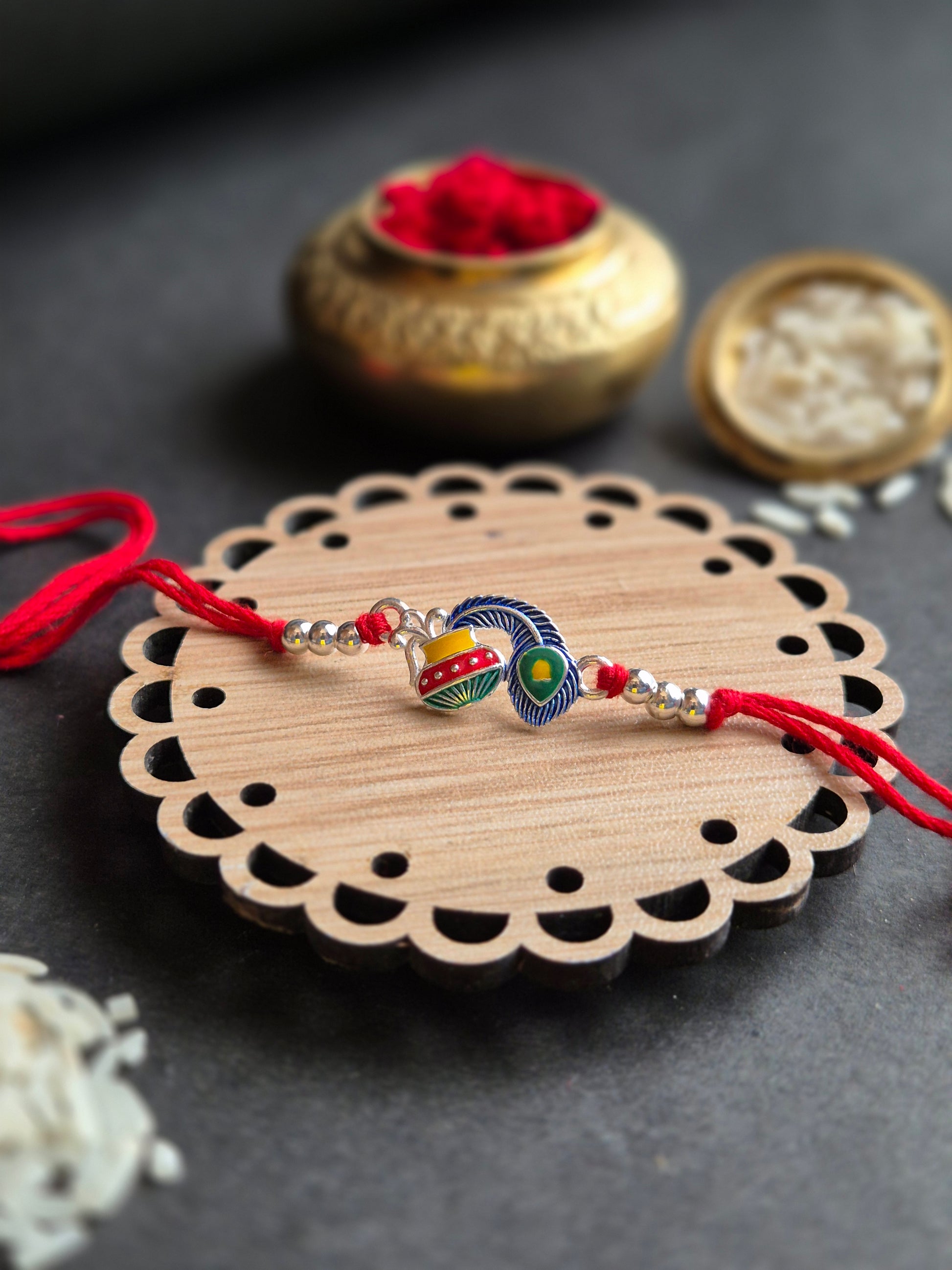 Divine Makhan Matka Sterling Silver Rakhi with red thread, symbolizing Krishna's love, on a decorative wooden stand.