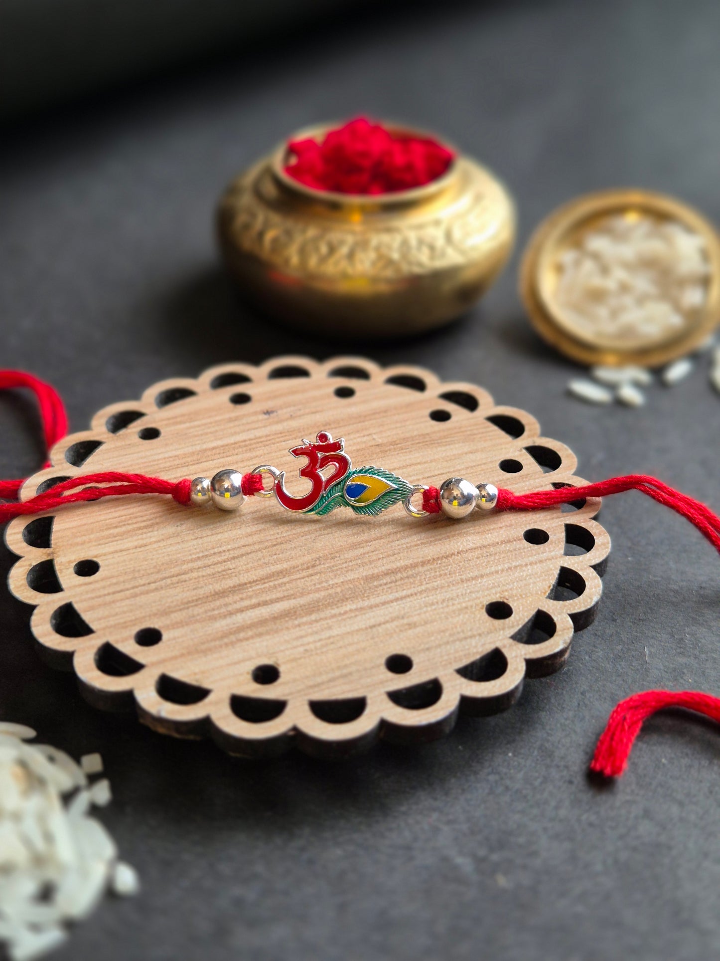 Elegant Om feather sterling silver rakhi on a decorative wooden base with red thread and rice for Raksha Bandhan.