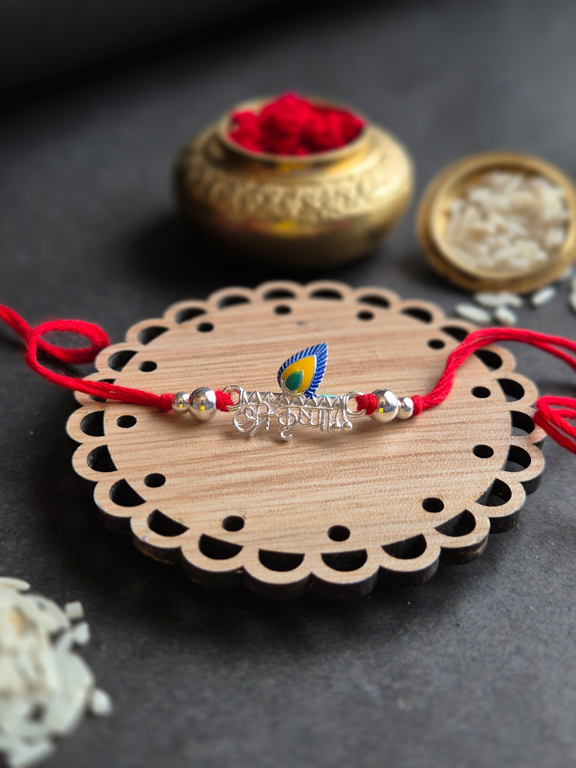 Divine Kanha sterling silver rakhi on a wooden plate, adorned with red threads and decorative elements for Raksha Bandhan.