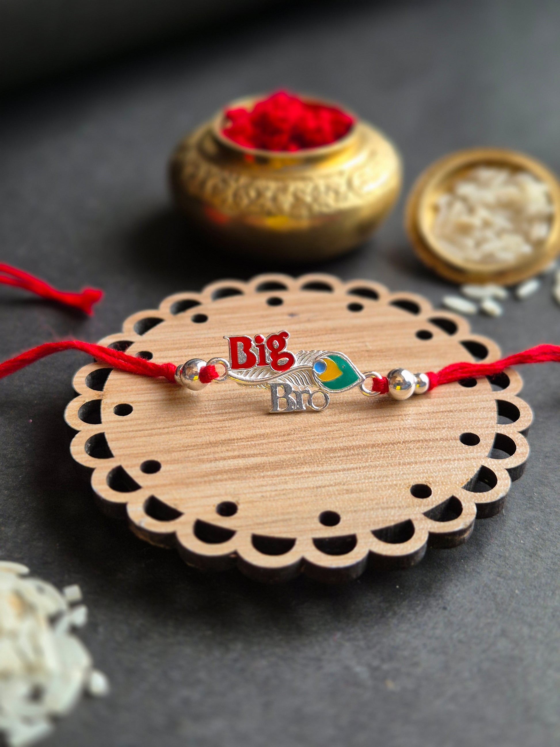 Handmade Big Bro Sterling Silver Rakhi with red thread and enameled feather on decorative wooden plate.