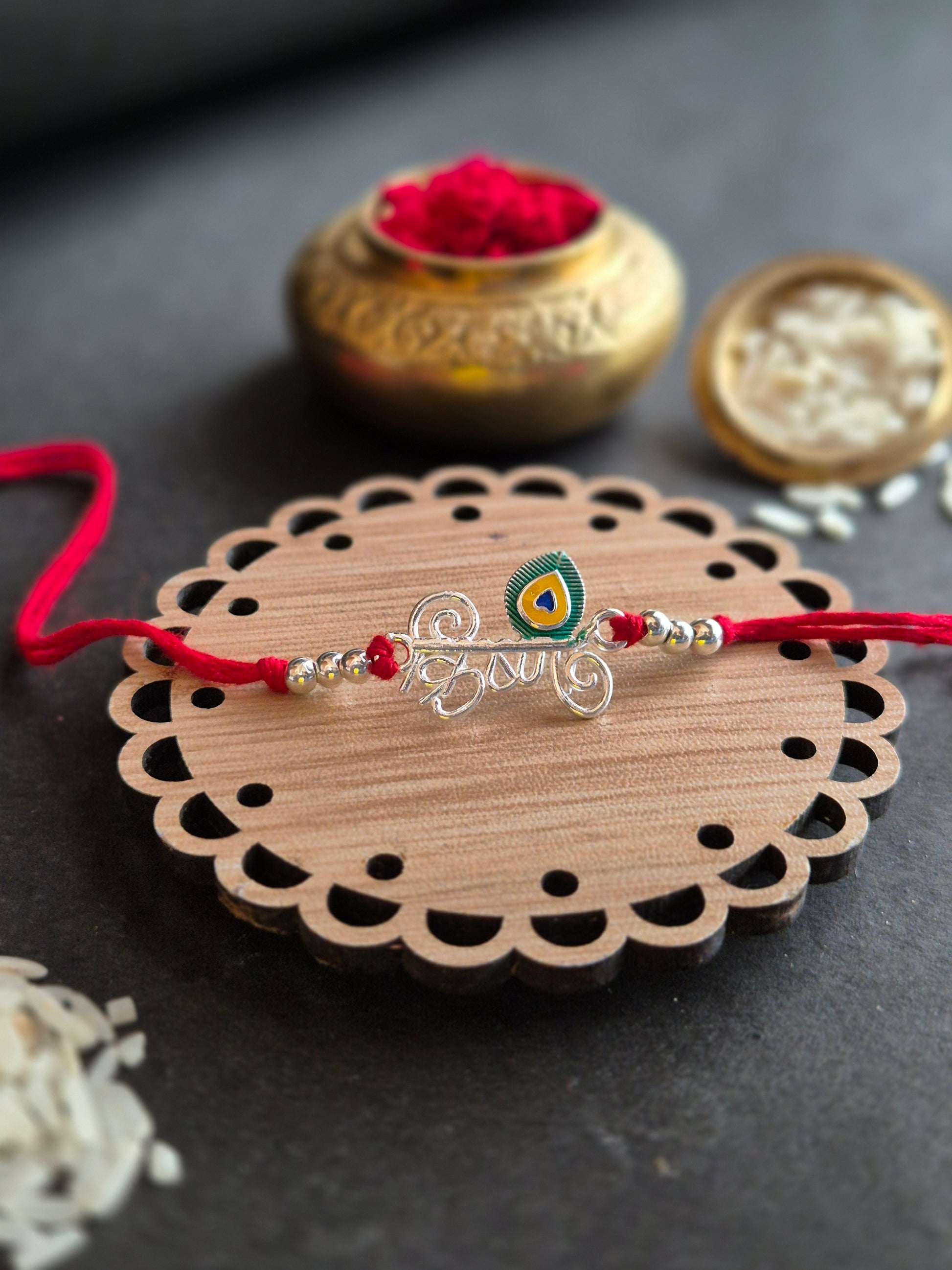 Krishna Sterling Silver Rakhi with peacock feather on decorative wooden surface for Raksha Bandhan celebration.