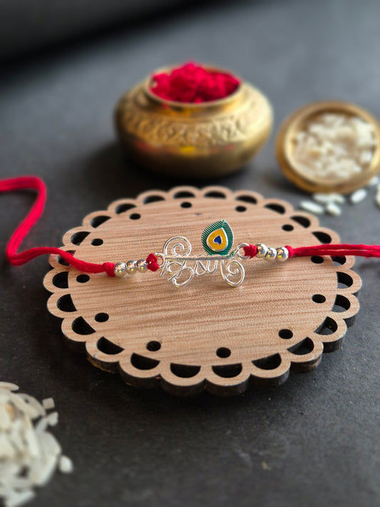 Krishna Sterling Silver Rakhi with peacock feather on decorative wooden surface for Raksha Bandhan celebration.