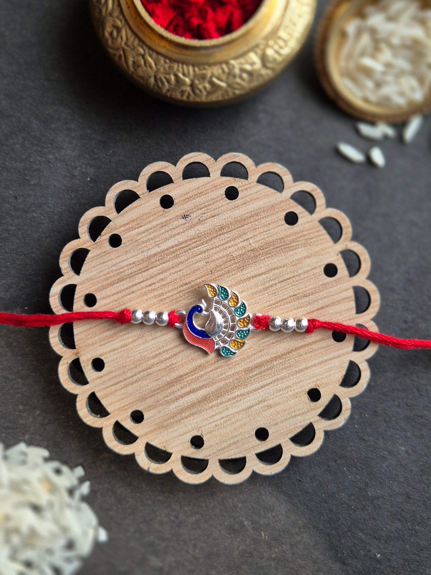 Majestic Peacock Sterling Silver Rakhi featuring colorful enamel work on wooden base, symbolizing grace and good fortune.