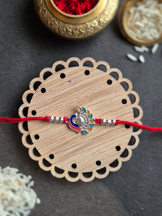 Majestic Peacock Sterling Silver Rakhi featuring colorful enamel work on wooden base, symbolizing grace and good fortune.