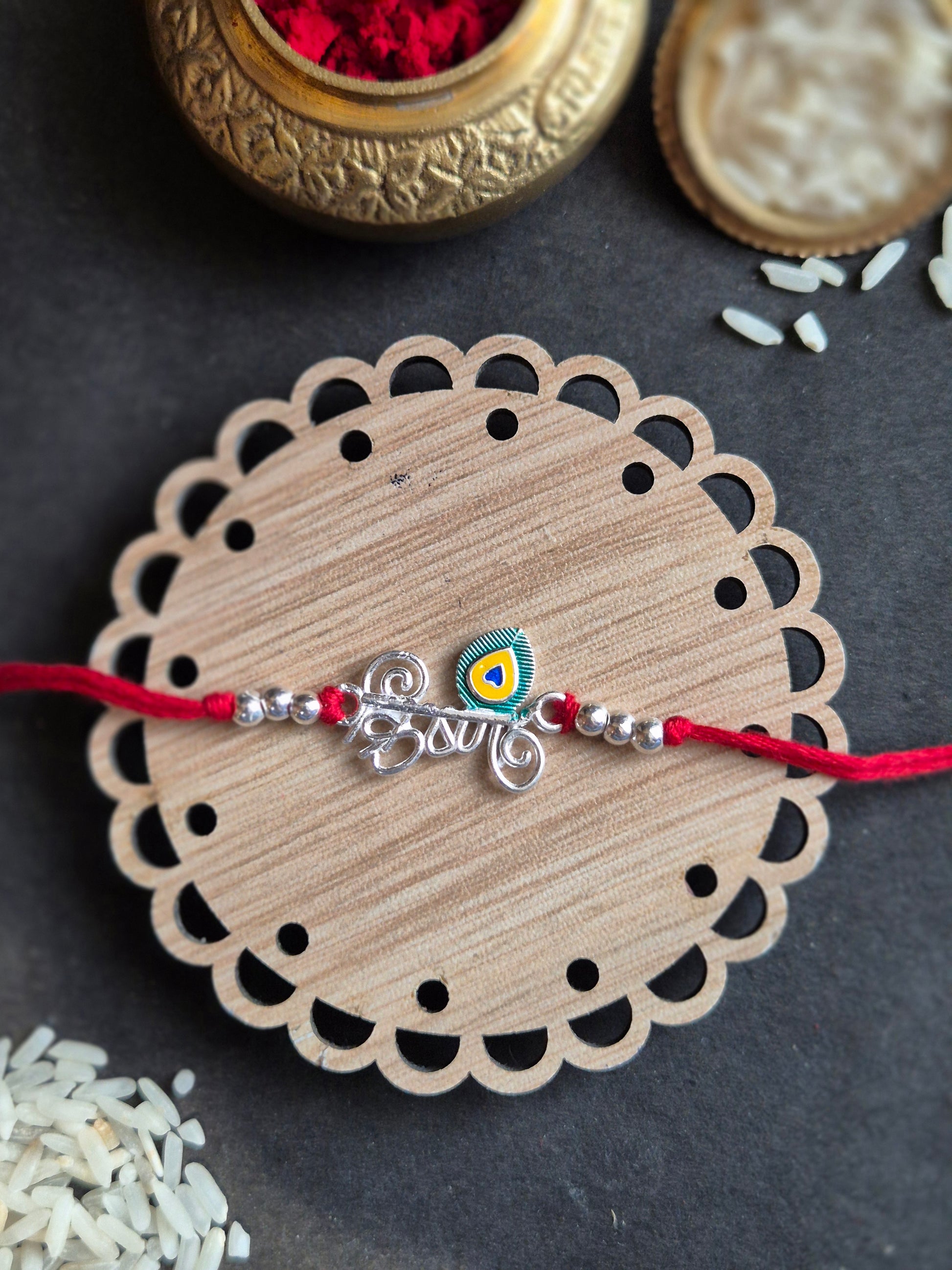 Sterling silver Rakhi with peacock feather design on wooden plate, perfect for Raksha Bandhan celebration.