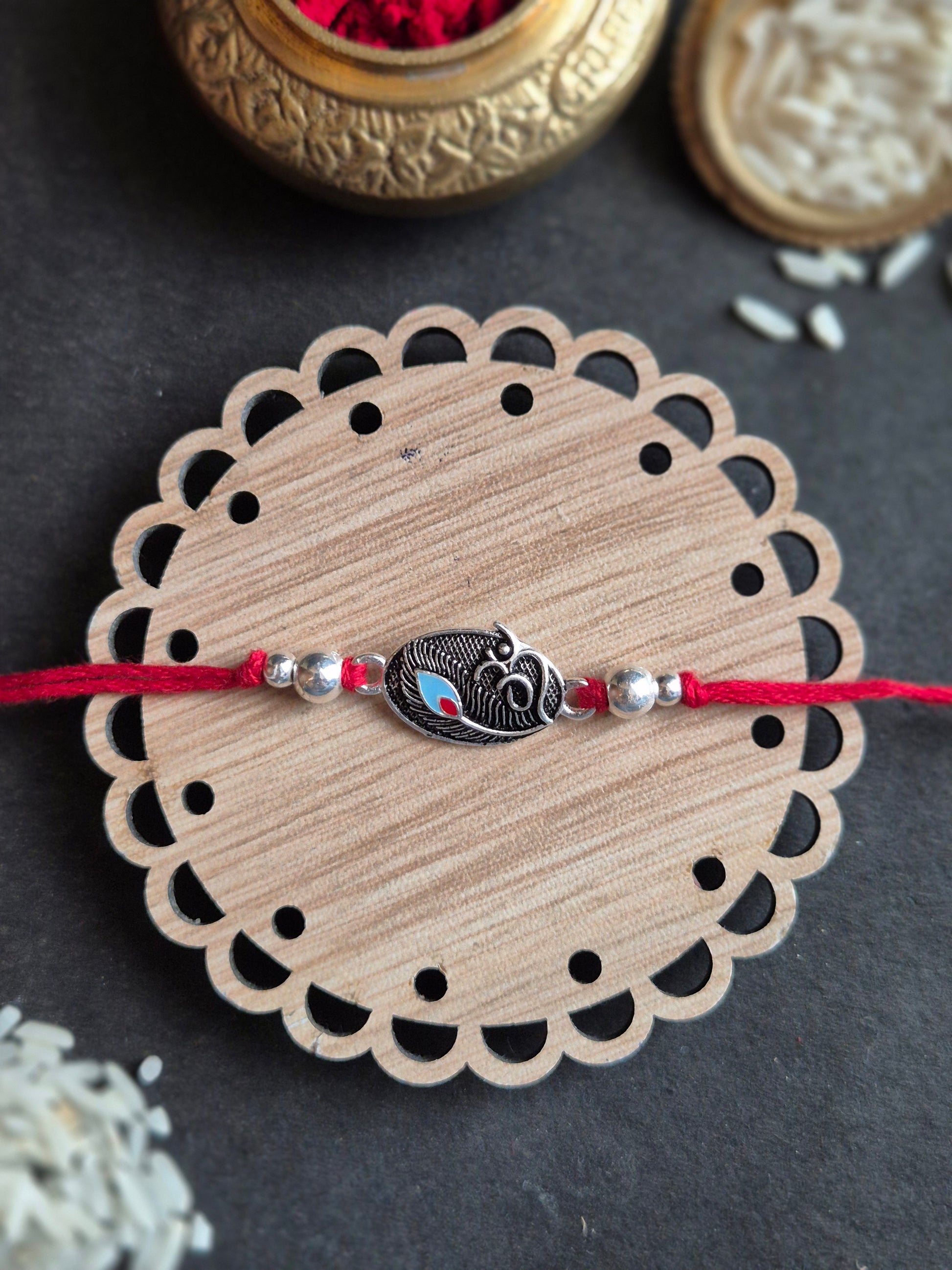 Handmade silver Rakhi with a central Om motif on a decorative wooden base for Raksha Bandhan.