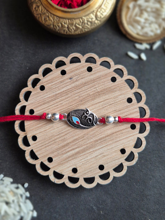 Handmade silver Rakhi with a central Om motif on a decorative wooden base for Raksha Bandhan.