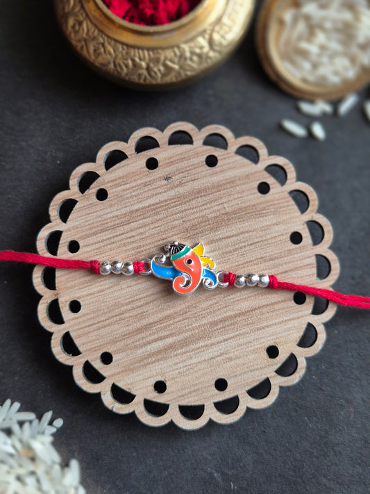 Vibrant Ganesha sterling silver rakhi with colorful design on a wooden base, perfect for Raksha Bandhan celebrations.