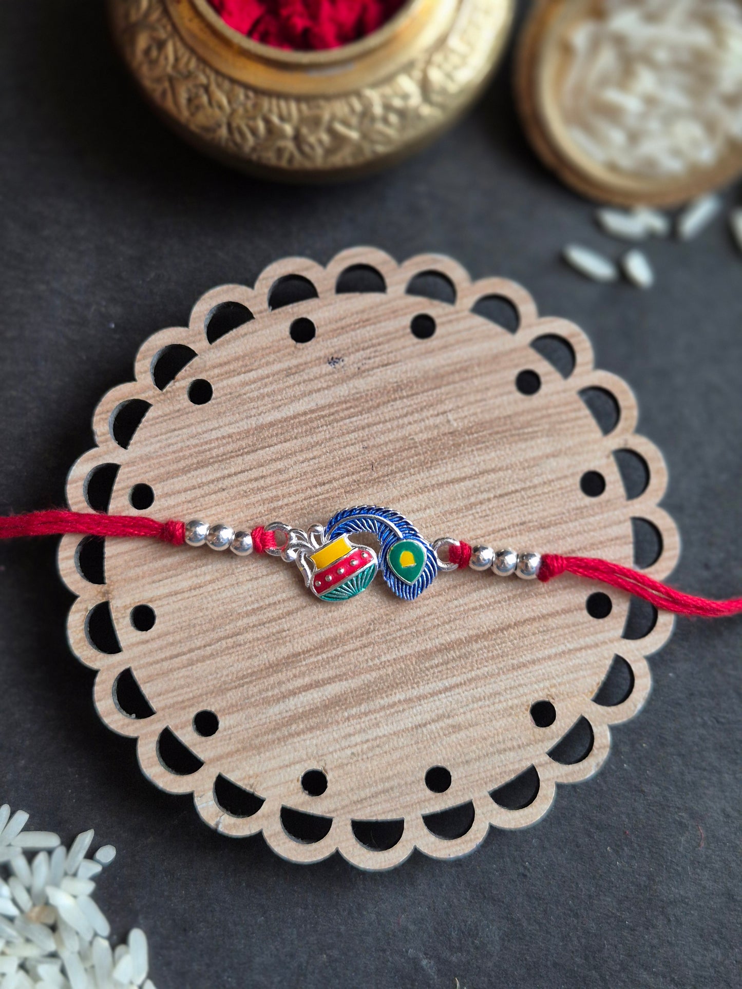 Divine Makhan Matka Sterling Silver Rakhi with colorful charms on wooden base for Raksha Bandhan celebration.
